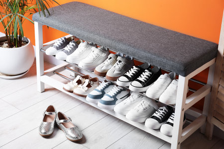 Different kid's shoes, storage bench and houseplant near orange wall indoorsの写真素材