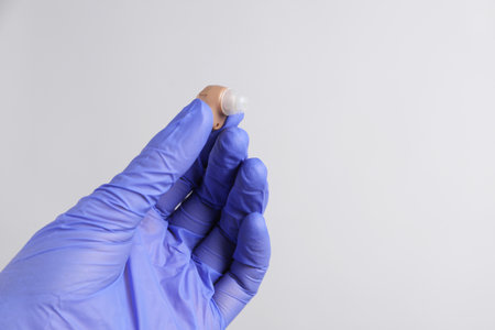 Doctor with hearing aid on light gray background, closeup.