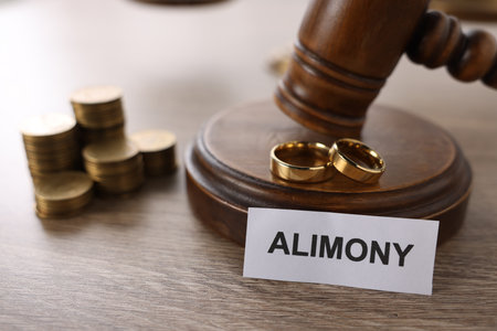 Paper note with word Alimony, wedding rings, judge's gavel and coins on wooden table, closeupの写真素材