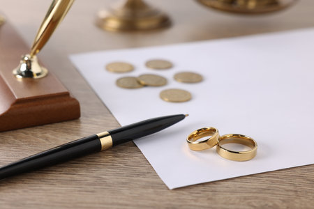 Alimony. Wedding rings, pen, coins and document on wooden table, closeupの写真素材
