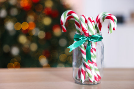 Merry Christmas and Happy New Year. Jar with tasty candy canes on light wooden table against blurred lights, closeup. Space for textの写真素材