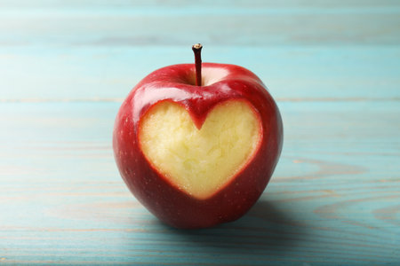 Red apple with carved heart on blue wooden table, closeupの写真素材