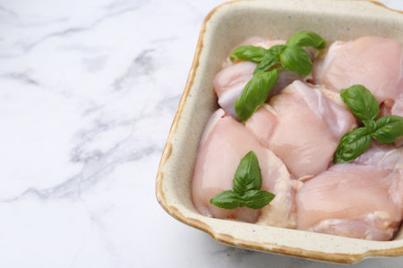 Raw chicken thighs with basil in baking dish on white marble table, closeup. Space for textの写真素材