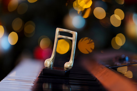 Golden music note on piano against blurred Christmas lights, closeup. Bokeh effectの写真素材