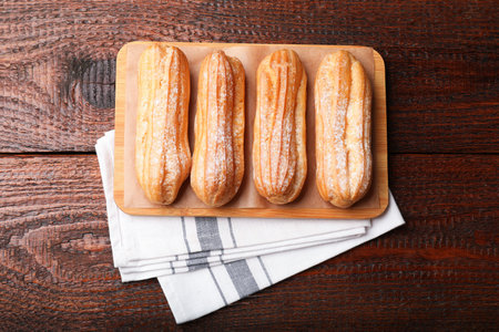 Tasty eclairs with powdered sugar on wooden table, top view