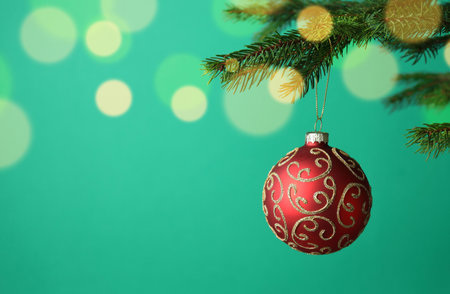 Red Christmas ball with pattern hanging on fir tree branch against green background with blurred lights, closeup with space for text. Bokeh effectの写真素材