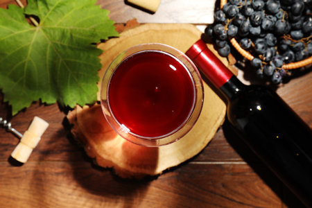 Red wine in glass, bottle, corkscrew and grapes on wooden table, flat layの写真素材