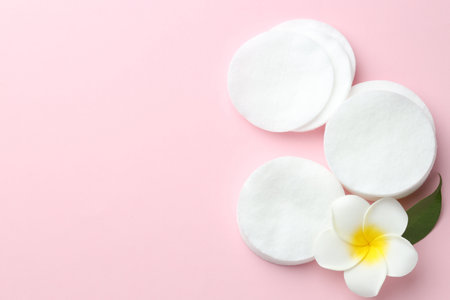 Clean cotton pads and plumeria flower on pink background, flat lay. Space for textの写真素材