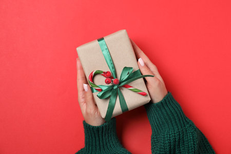 Woman holding decorated Christmas gift with candy cane on red background, top viewの写真素材