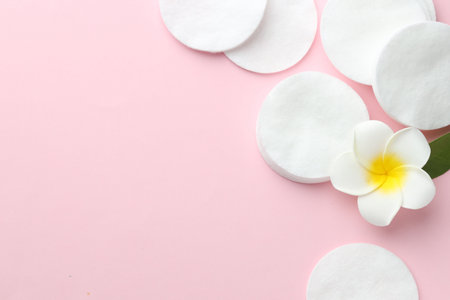 Clean cotton pads and plumeria flower on pink background, flat lay. Space for textの写真素材