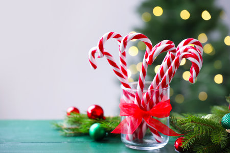Candy canes in glass and Christmas decor on green wooden table against blurred lights. Space for textの写真素材