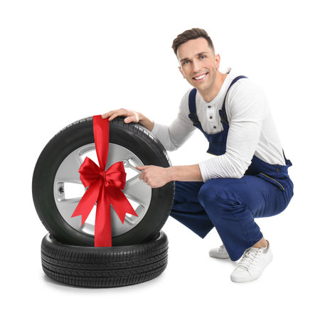 Tire service worker and car wheel with red ribbon bow on white background.の写真素材