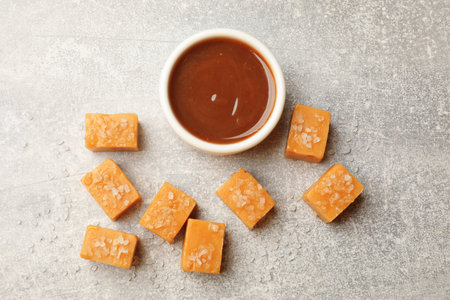 Tasty candies with salt and caramel sauce on gray textured table, flat layの写真素材