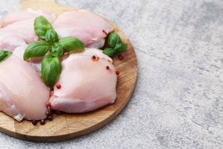 Raw chicken thighs with basil and peppercorns on light table, closeup. Space for textの写真素材