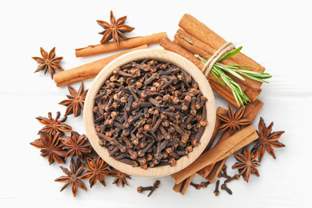 Mulled wine spices. Cloves in bowl, anise stars, cinnamon sticks and fresh rosemary on white wooden table, flat layの写真素材