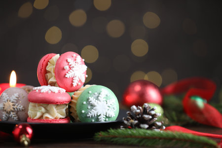 Tasty macarons and Christmas decor on black wooden table against blurred lights, closeup. Space for textの写真素材