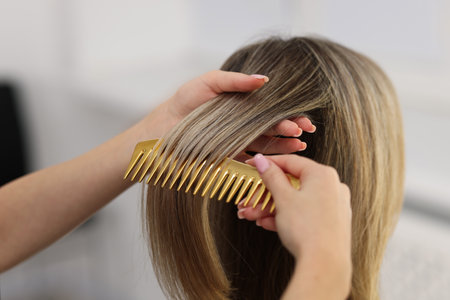 Hairdresser combing woman's hair in salon, closeupの写真素材
