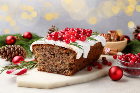Tasty Christmas cake with icing, cranberries, nuts and festive decor on light gray table against...