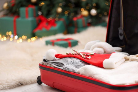 Christmas vacation. Suitcase with Santa hat, clothes and candy canes on floor indoors, closeup. Space for textの写真素材