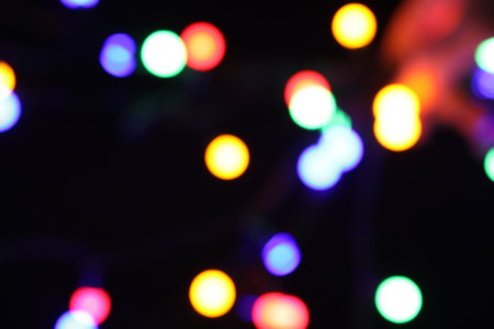 Blurred view of bright Christmas lights on dark background, bokeh effect