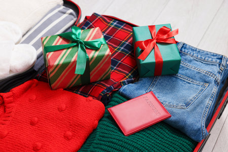 Christmas vacation. Suitcase with Santa hat, clothes and gift boxes on floor indoors, closeupの写真素材