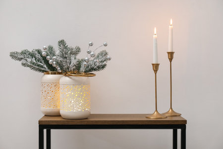 Christmas decor and burning candles on console table near white wall indoors