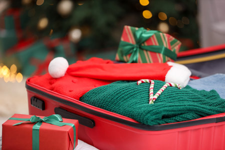 Christmas vacation. Suitcase with Santa hat, clothes, candy canes and gift box on floor indoors, closeupの写真素材