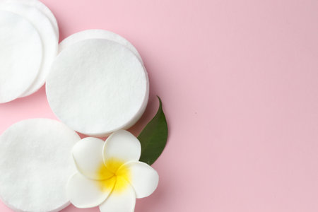 Clean cotton pads and plumeria flower on pink background, flat lay. Space for textの写真素材