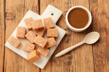 Tasty candies with salt, caramel sauce and spoon on wooden table, flat layの写真素材