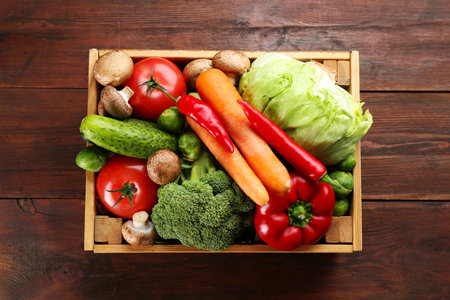 Different fresh raw vegetables in crate on wooden table, top viewの写真素材