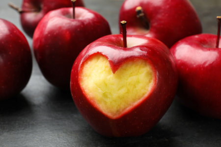 Red apple with carved heart and other fruits on black table, closeupの写真素材