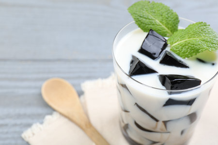 Glass of milk with tasty herbal jelly and mint on gray wooden table, closeup. Space for textの写真素材