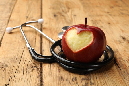 Apple with carved heart and stethoscope on wooden table, closeupの写真素材