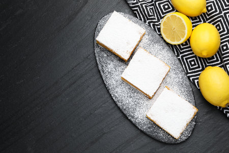Tasty lemon bars and fresh fruits on black table, flat lay. Space for textの写真素材