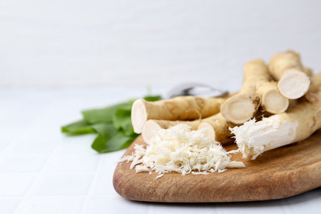 Grated horseradish and fresh roots on white tiled table, closeup. Space for textの写真素材