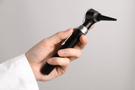 Doctor with otoscope on light gray background, closeupの写真素材