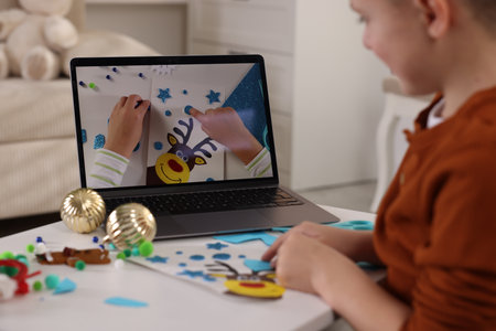Little boy making Christmas postcard by video tutorial at table indoors, selective focus. Child...