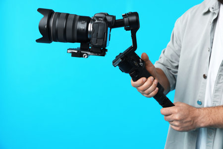 Videographer using gimbal stabilizer with camera on light blue background, closeup