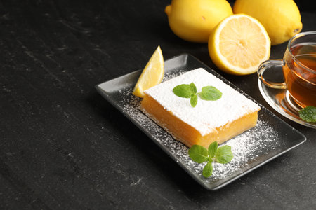 Tasty lemon bar with mint, fresh fruits and tea on black table, closeup. Space for textの写真素材