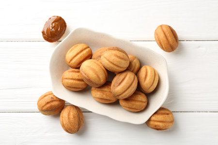 Delicious nut shaped cookies with boiled condensed milk on white wooden table, top view