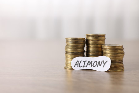 Paper note with word Alimony and stack of coins on wooden table, closeup. Space of textの写真素材