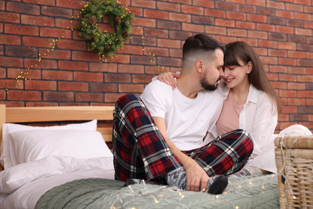 Happy couple in pajamas spending time together on bed in room decorated for Christmasの写真素材