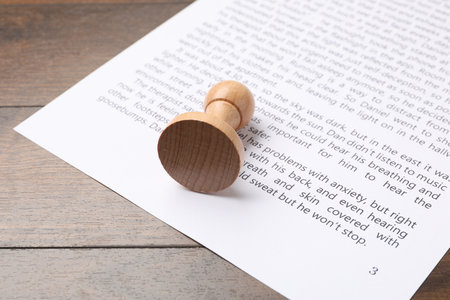 One wooden stamp and sheet of paper with text on table, closeupの写真素材