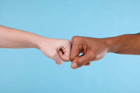 African American man bumping fists with his partner on light blue background, closeupの写真素材