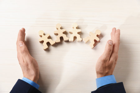 Man protecting human figures at white wooden table, above viewの写真素材