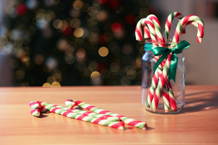 Merry Christmas and Happy New Year. Jar with tasty candy canes on light wooden table against blurred lights, closeupの写真素材