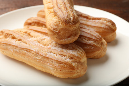 Tasty eclairs with powdered sugar on wooden table, closeup