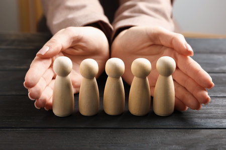 Woman protecting human figures at black wooden table, closeupの写真素材