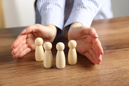 Woman protecting human figures at wooden table, closeupの写真素材