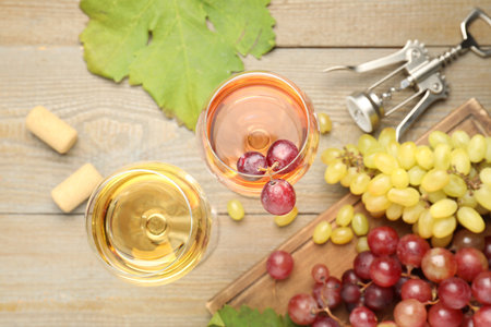 Tasty rose and white wine, grapes, corkscrew on wooden table, flat lay